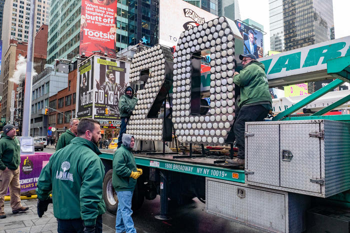 Workers remove the A couple poses in front of the 2 and 0 numerals for New Year's Eve in Times Square from a truck