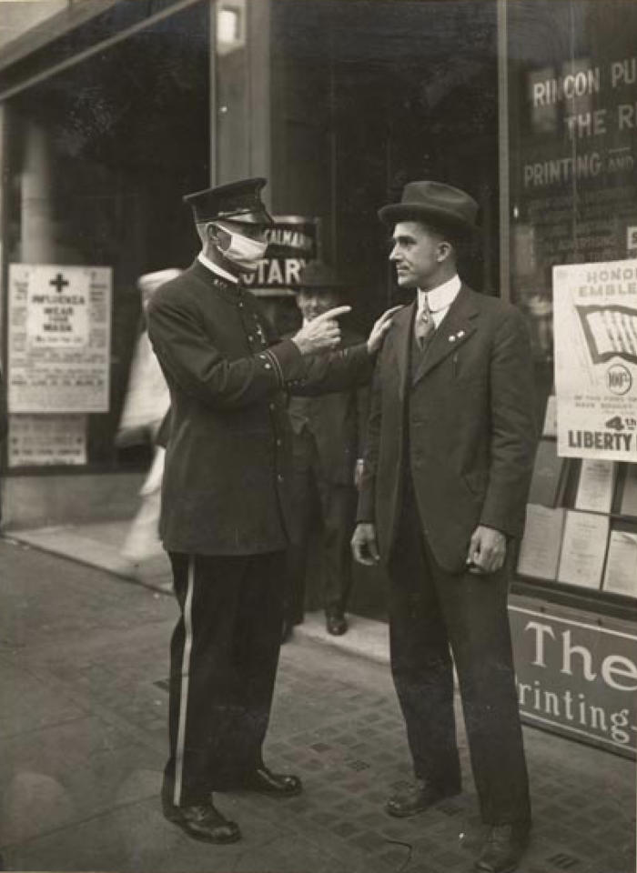 A policemaan wearing a flu mask speaks to a maskless man