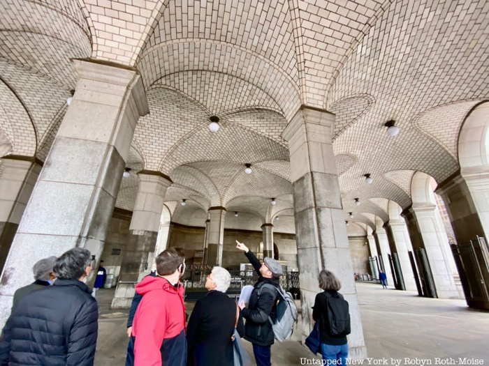 A group of tour guests look up at Guastavino tiles at the entrance to a subway station.