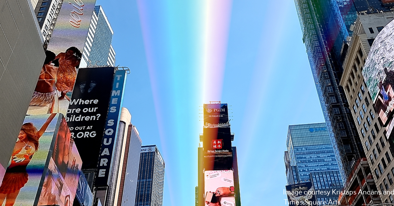 A rainbow made of light is visible in the sky over Times Square