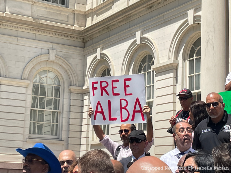 Man holding "Free Alba" sign during press conference on the steps of City Hall 
