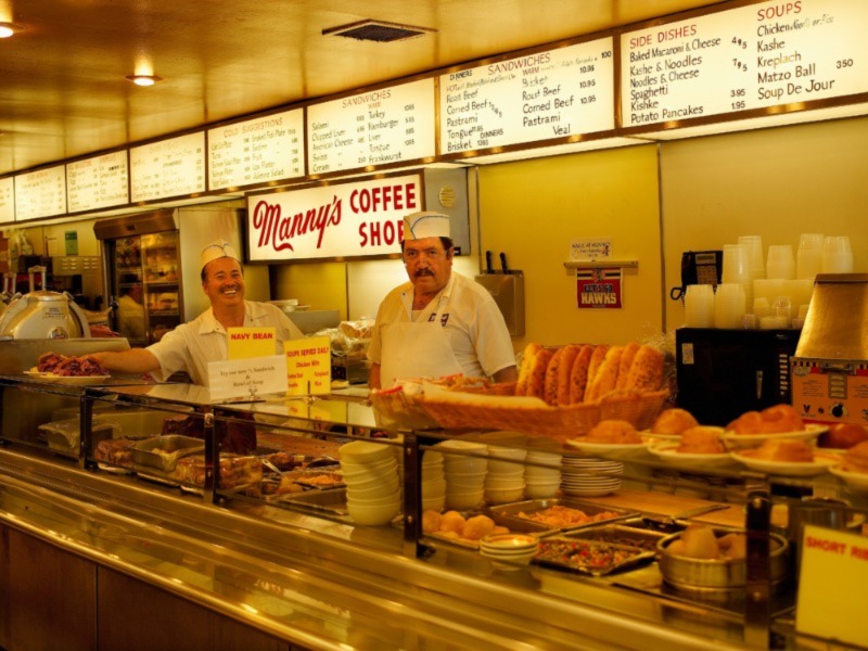 Two deli workers stand behind a counter of food at a jewish deli in Chicago.