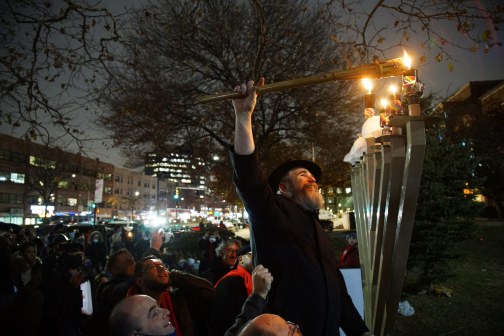 A man is lifted up by a crowd to light the flame of a giant menorah in Queens