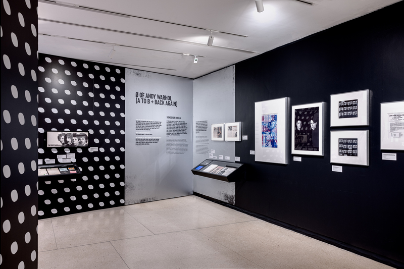 Black, grey and white polka dot walls covered in items related to The Velvet Underground and Andy Warhol at an NYPL exhibit