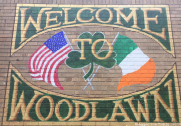 "Welcome to Woodlawn" painted sign on a brick wall with Irish and American flag