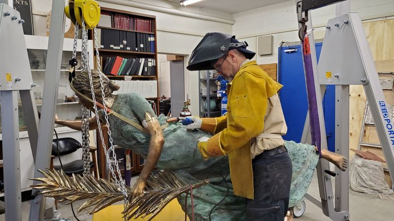 A man welds pieces of a bronze sculpture together