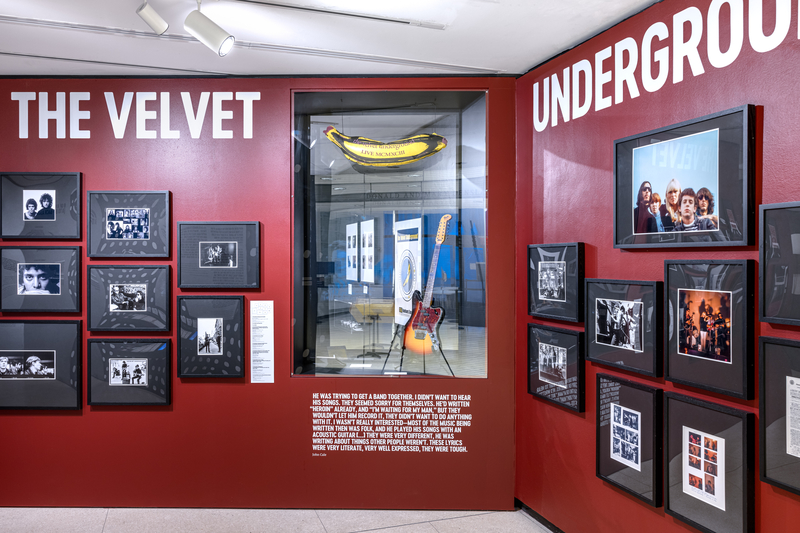 The Velvet Underground photos and promotional banana on display against a red wall at an NYPL exhibit