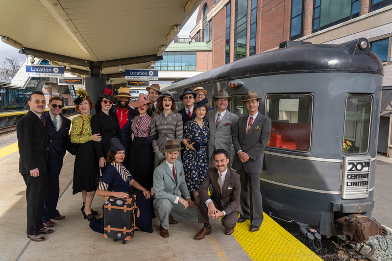 People dressed in vintage attire outside a vintage rail car on a train platform