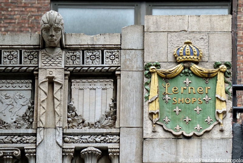 A carved sign for Lerner Shops on the side of a stone building next to other decorative carvings including a head with a helmet