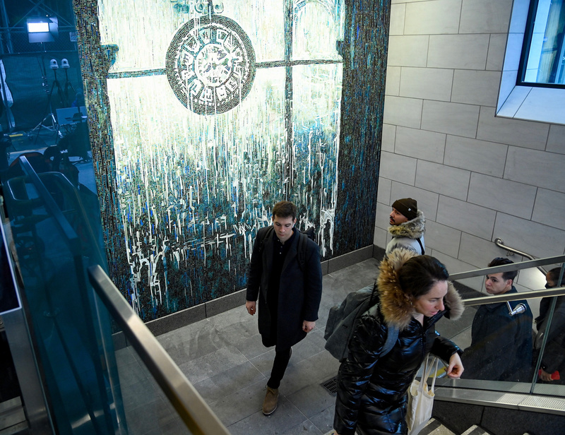 People walk up steps past New mosaic in Penn Station that depicts a clock framed by an arched window