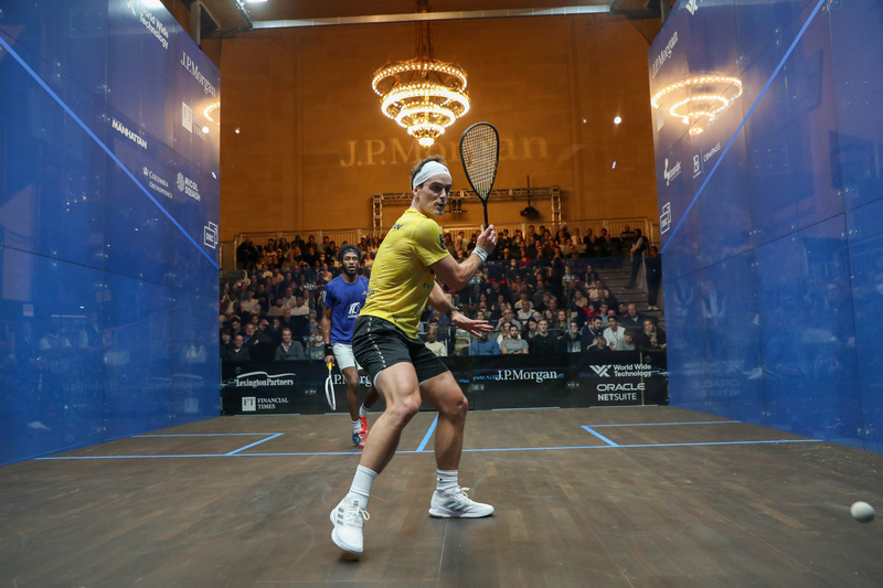 A squash player hits a ball inside the glass enclosed court at Grand Central Terminal