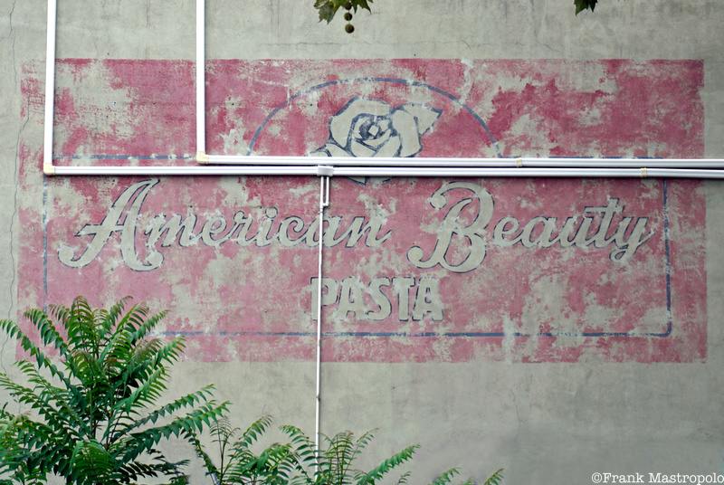 A fading painted sign that reads "American Beauty Pasta" in script on a pink background with a white rose on top