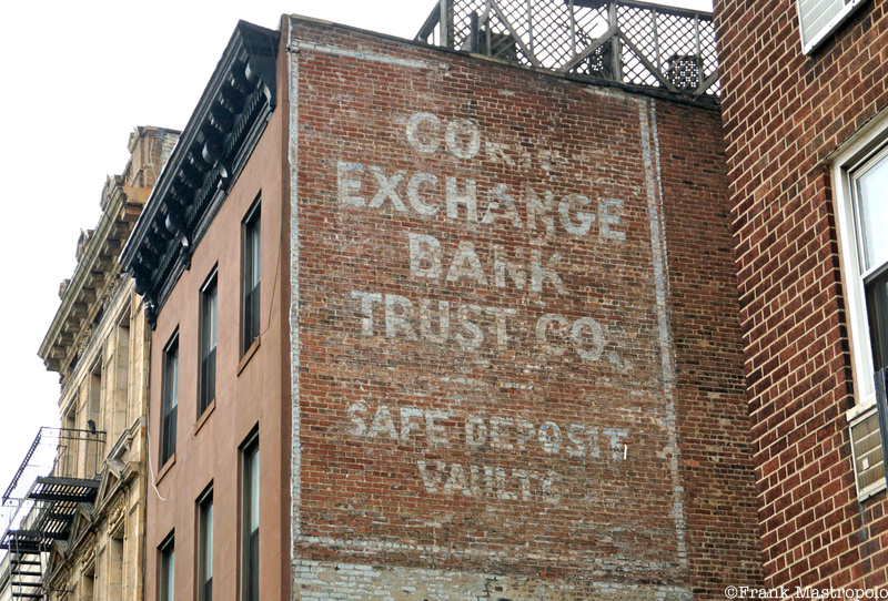 A fading ghost sign on the side of a brick wall that reads "Corn Exchange Bank Trust Co. Safe Deposit Vaults"