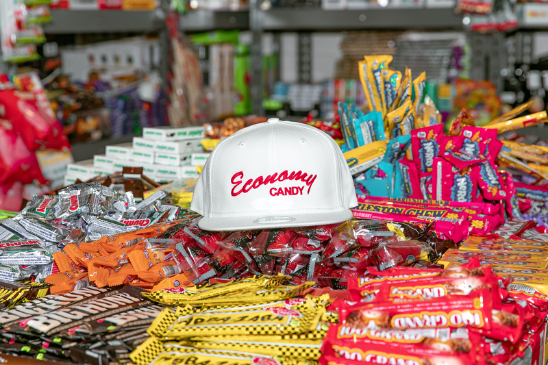 A white baseball cap  with the Economy Candy logo sits on top of a pile of colorful candies