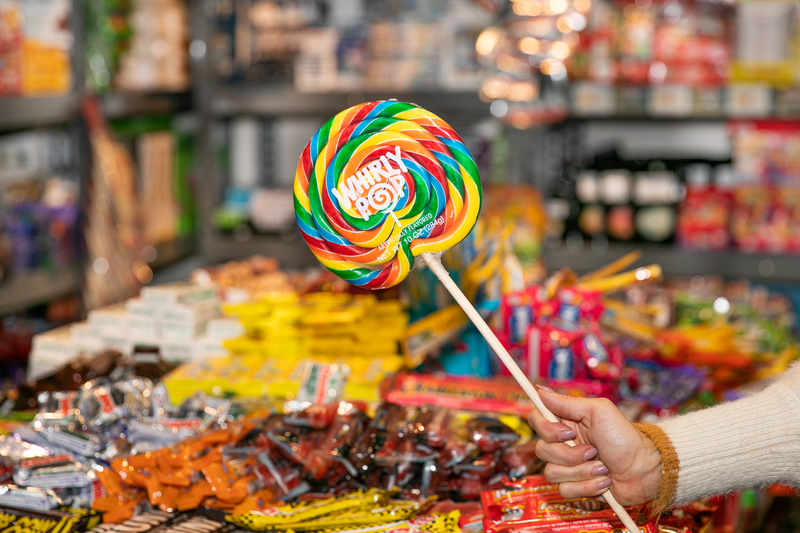 A large multi color spiral lollipop is held in front of a pile of packaged candies