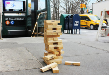 A stack of JENGA blocks on the sidewalk outside of an NYC subway station