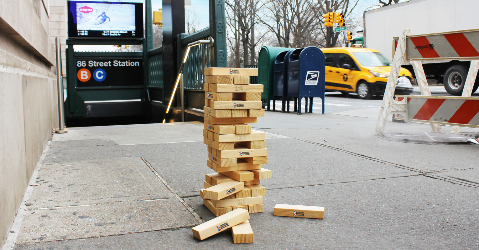 A stack of JENGA blocks on the sidewalk outside of an NYC subway station