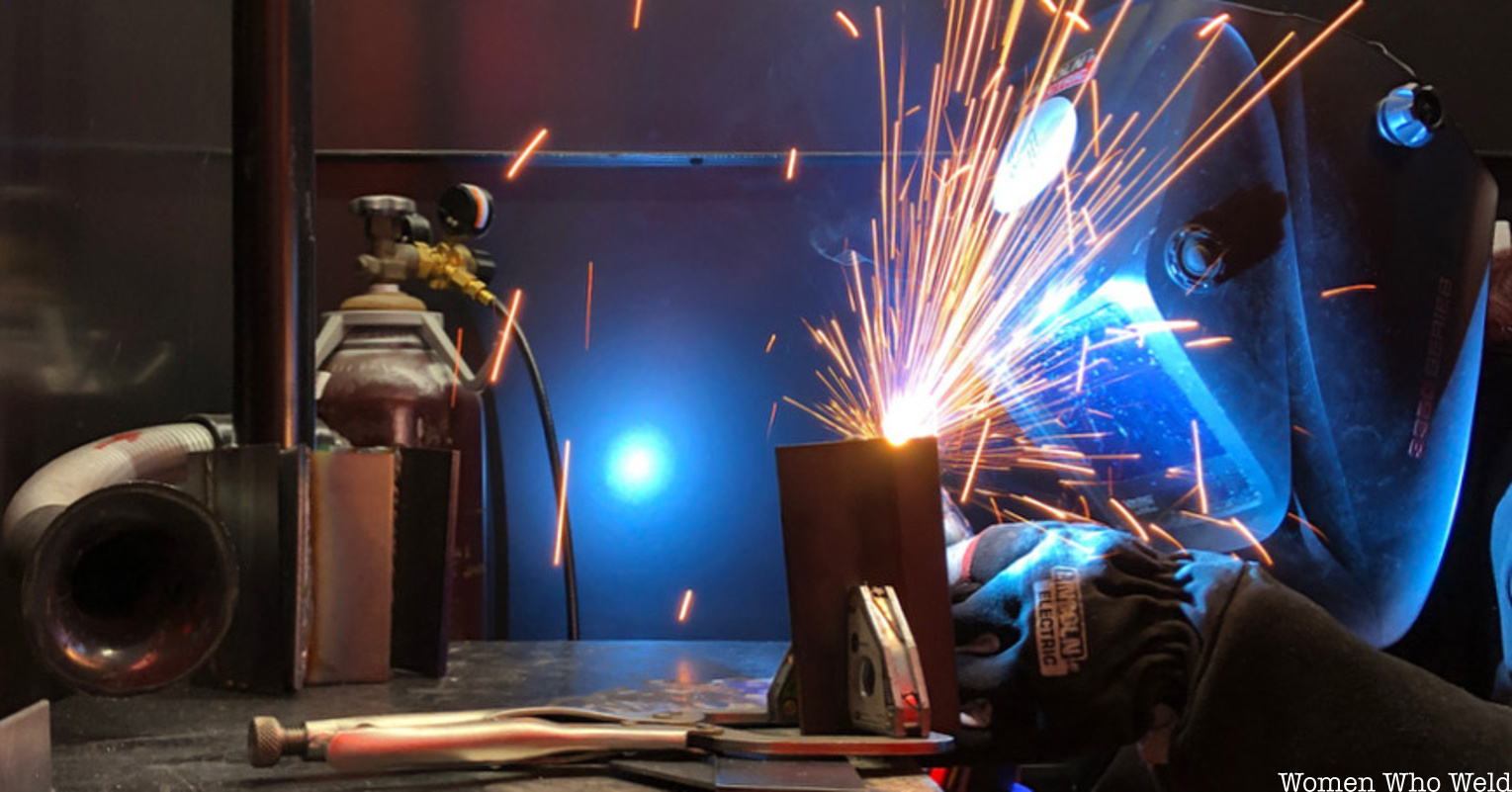 A women in a welding mask makes sparks as she welds