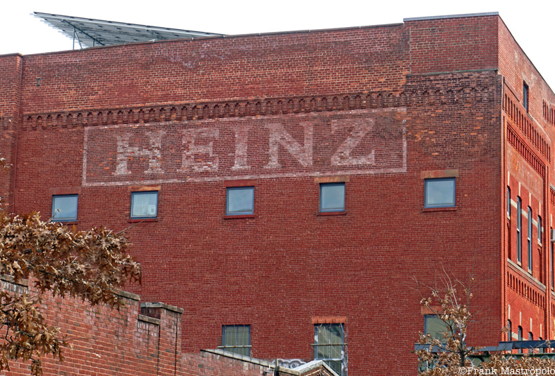 A fading ghost sign that says "Heinz" on a red brick building above a row of windows