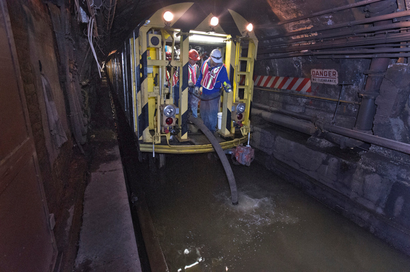 MTA workers hold a hose from a pump train to suck up flooding waters inside a tunnel