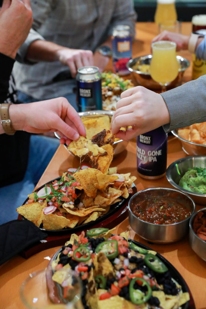 Hands picking up chips in a plate of nachos at Hudson Yards Bronx Brewery location