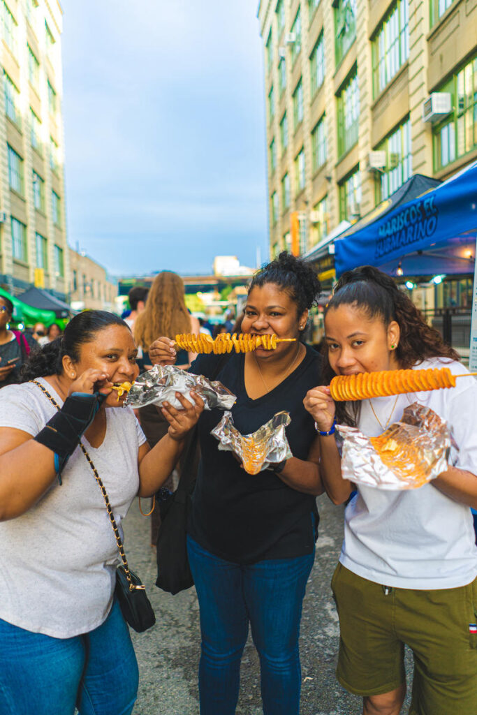 Three women eat food at the Brooklyn Night Market at Industry City