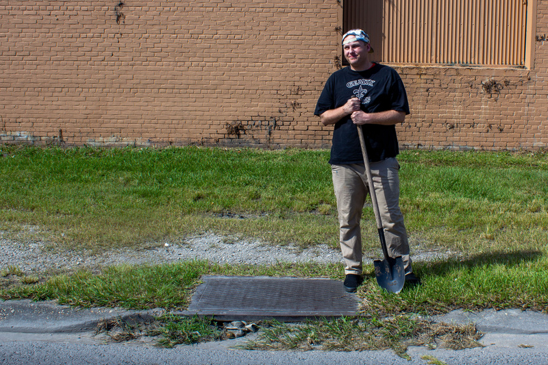 New Orleans Sewage and Water boy stands by a storm drain with a shovel