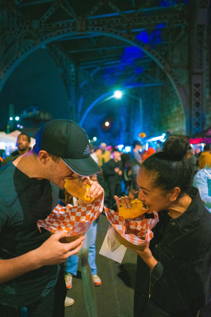 A couple of people biting into food at the Uptown Night Market