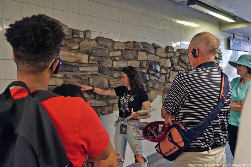 Tourgoers on a Remnants of Dutch New Amsterdam tour touch a stone wall in the subway