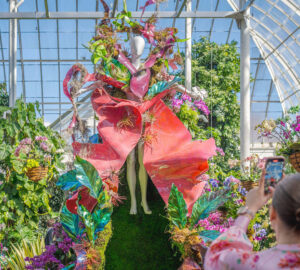Woman takes a photo of a mannequin surrounded by floral displays